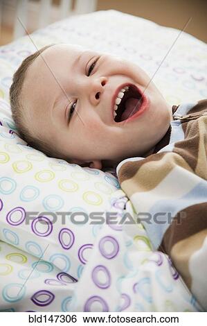 Stock Photograph - Laughing Caucasian boy laying in bed. Fotosearch