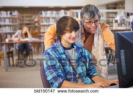 Stock Photo - Librarian helping boy with computer in library. Fotosearch