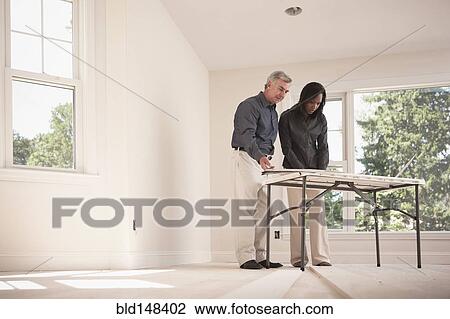 Stock Image - Man and woman looking at blueprints together. Fotosearch