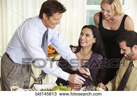 Stock Image - Man serving friends salad at dinner party. Fotosearch