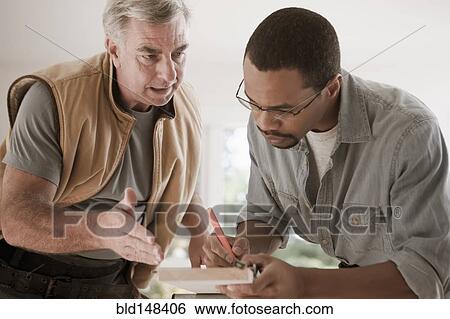 Stock Photograph - Man talking to carpenter measuring lumber. Fotosearch