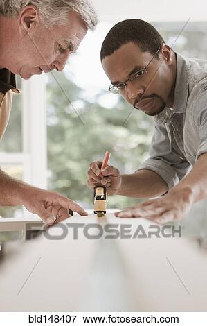 Stock Photo - Man watching carpenter measuring lumber. Fotosearch