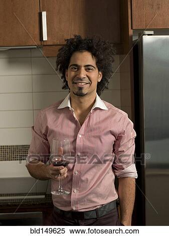 Stock Photography - Middle Eastern man drinking red wine in kitchen. Fotosearch
