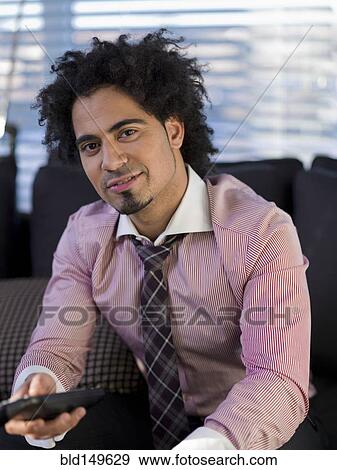 Stock Photo - Middle Eastern man watching television on sofa. Fotosearch