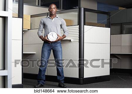 Mixed race businessman holding clock in office cubicle View Large Photo Image Picture - Mixed race businessman holding clock in office cubicle. Fotosearch