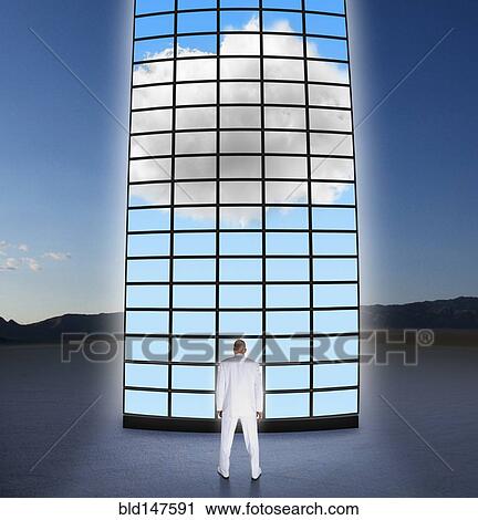 Stock Image - Mixed race businessman looking at towering monitors. Fotosearch