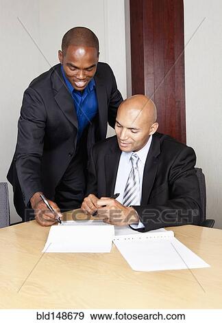 Stock Photo - Mixed race businessmen reviewing contract in conference room. Fotosearch