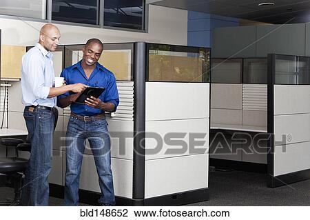 Stock Image - Mixed race businessmen using digital tablet in office. Fotosearch