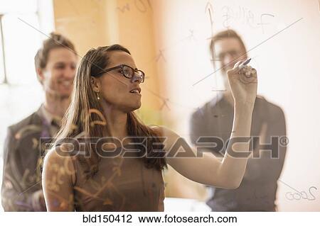 Stock Image - Mixed race businesswoman writing on glass wall. Fotosearch