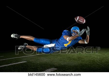 Stock Image - Mixed race football player jumping in mid-air catching football. Fotosearch