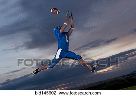 Stock Image - Mixed race football player jumping in mid-air catching football. Fotosearch