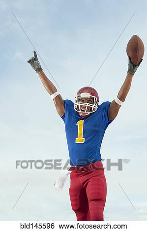 Stock Photograph - Mixed race football player with arms raised holding football. Fotosearch
