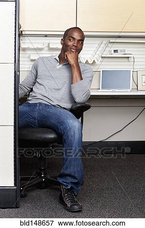 Stock Photo - Mixed race man sitting in office cubicle. Fotosearch