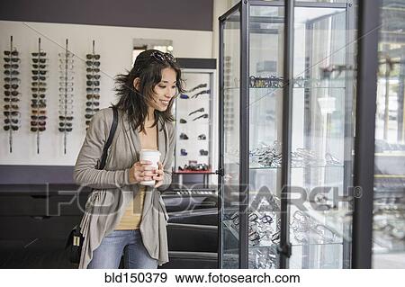 Mixed race woman drinking coffee and looking at eyeglasses in shop View Large Photo Image Stock Photo - Mixed race woman drinking coffee and looking at eyeglasses in shop. Fotosearch