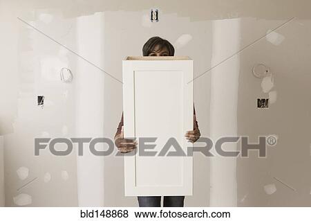 Stock Photo - Mixed race woman holding cabinet door in unfinished room. Fotosearch