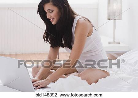 Stock Image - Mixed race woman using laptop in bed. Fotosearch