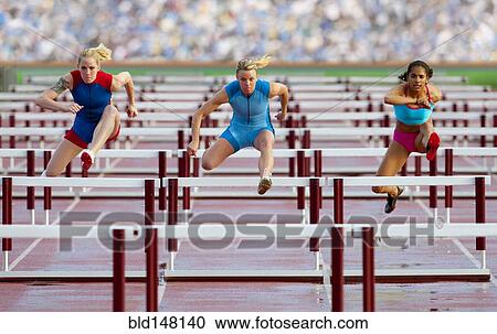 Stock Image - Runners jumping hurdles in race. Fotosearch