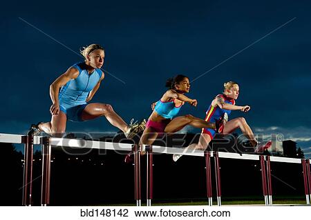 Stock Image - Runners jumping hurdles in race. Fotosearch