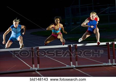 Stock Image - Runners jumping hurdles in race. Fotosearch