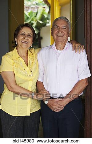 Stock Image - Senior Hispanic couple hugging in doorway. Fotosearch