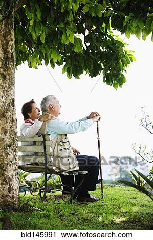 Senior Hispanic couple sitting on park bench View Large Photo Image Stock Image - Senior Hispanic couple sitting on park bench. Fotosearch