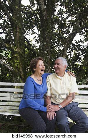 Stock Photo - Senior Hispanic couple sitting on park bench. Fotosearch