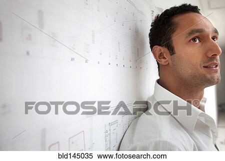 Stock Photography - Serious Hispanic businessman leaning against blueprint. Fotosearch