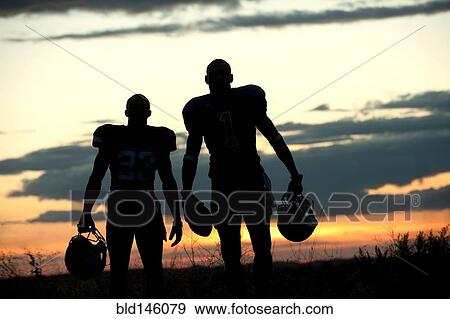 Stock Photo - Silhouette of Black football players carrying helmet and football. Fotosearch