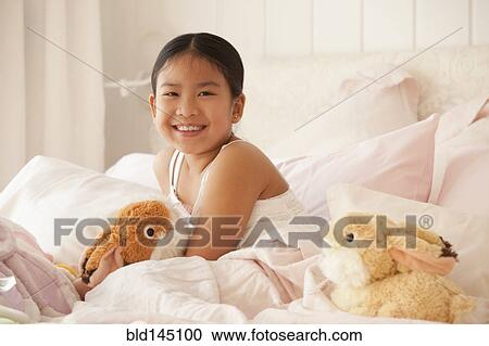 Stock Image - Smiling Asian girl laying in bed. Fotosearch