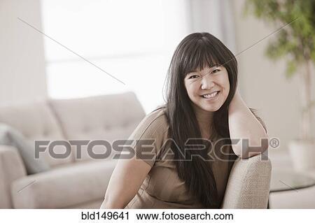 Stock Image - Smiling Asian woman in living room. Fotosearch
