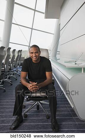 Smiling Black businessman sitting in conference room View Large Photo Image Stock Photo - Smiling Black businessman sitting in conference room. Fotosearch