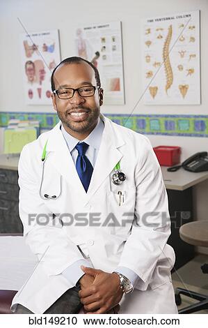 Stock Image - Smiling Black doctor sitting in doctor's office. Fotosearch