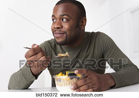 Stock Image - Smiling Black man eating breakfast. Fotosearch