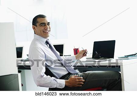 Smiling businessman sitting at desk View Large Photo Image Stock Image - Smiling businessman sitting at desk. Fotosearch