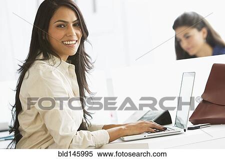 Stock Photography - Smiling businesswoman typing on laptop in office. Fotosearch