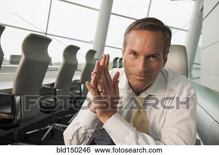 Stock Photograph - Smiling Caucasian businessman sitting in conference room. Fotosearch