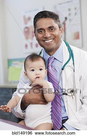 Smiling doctor holding baby in doctor's office View Large Photo Image Stock Photograph - Smiling doctor holding baby in doctor's office. Fotosearch