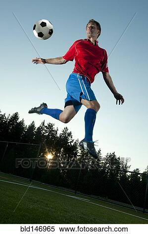 Stock Photography - Soccer player jumping in mid-air kicking ball. Fotosearch