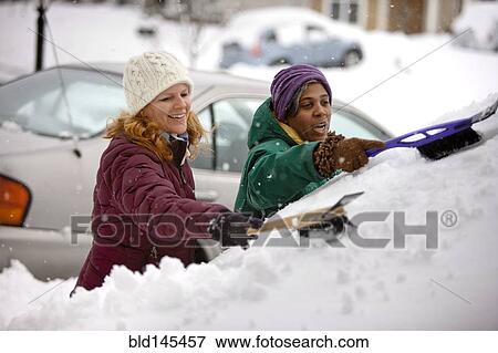 Stock Photo - Two women scraping snow from windshield. Fotosearch