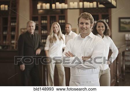 Stock Image - Wait staff and owner standing in restaurant. Fotosearch