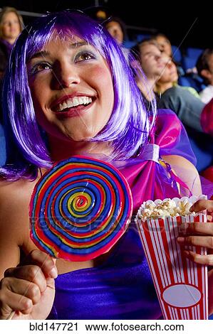 Stock Image - Woman eating candy and popcorn in movie theater. Fotosearch