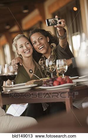 Stock Image - Women taking self-portrait in restaurant. Fotosearch