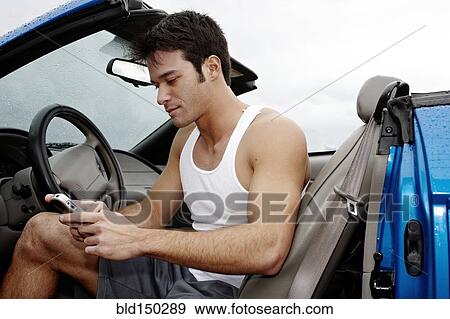 Young man sitting in car text messaging on cell phone View Large Photo Image Stock Photo - Young man sitting in car text messaging on cell phone. Fotosearch