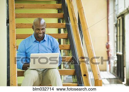 Picture - Black businessman using laptop on staircase. Fotosearch