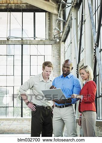 Stock Image - Business people using laptop in warehouse. Fotosearch