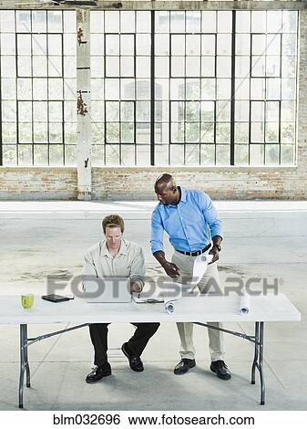 Businessmen reading blueprints in empty warehouse View Large Photo Image Stock Photograph - Businessmen reading blueprints in empty warehouse. Fotosearch