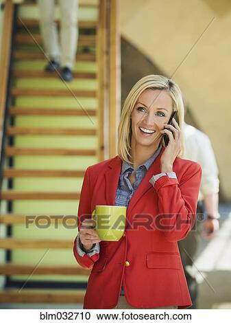 Stock Image - Businesswoman talking on cell phone near staircase. Fotosearch
