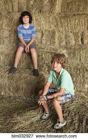 Stock Photo - Caucasian boys sitting on hay bales. Fotosearch