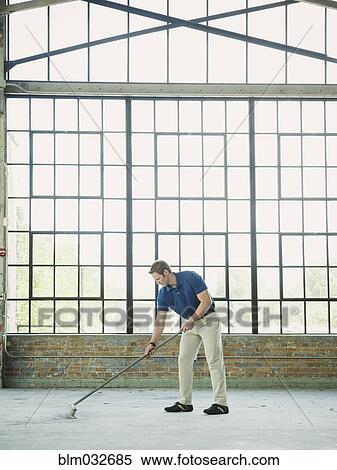 Stock Photography - Caucasian businessman sweeping warehouse floor. Fotosearch