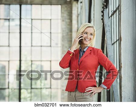 Stock Image - Caucasian businesswoman talking on cell phone in warehouse. Fotosearch
